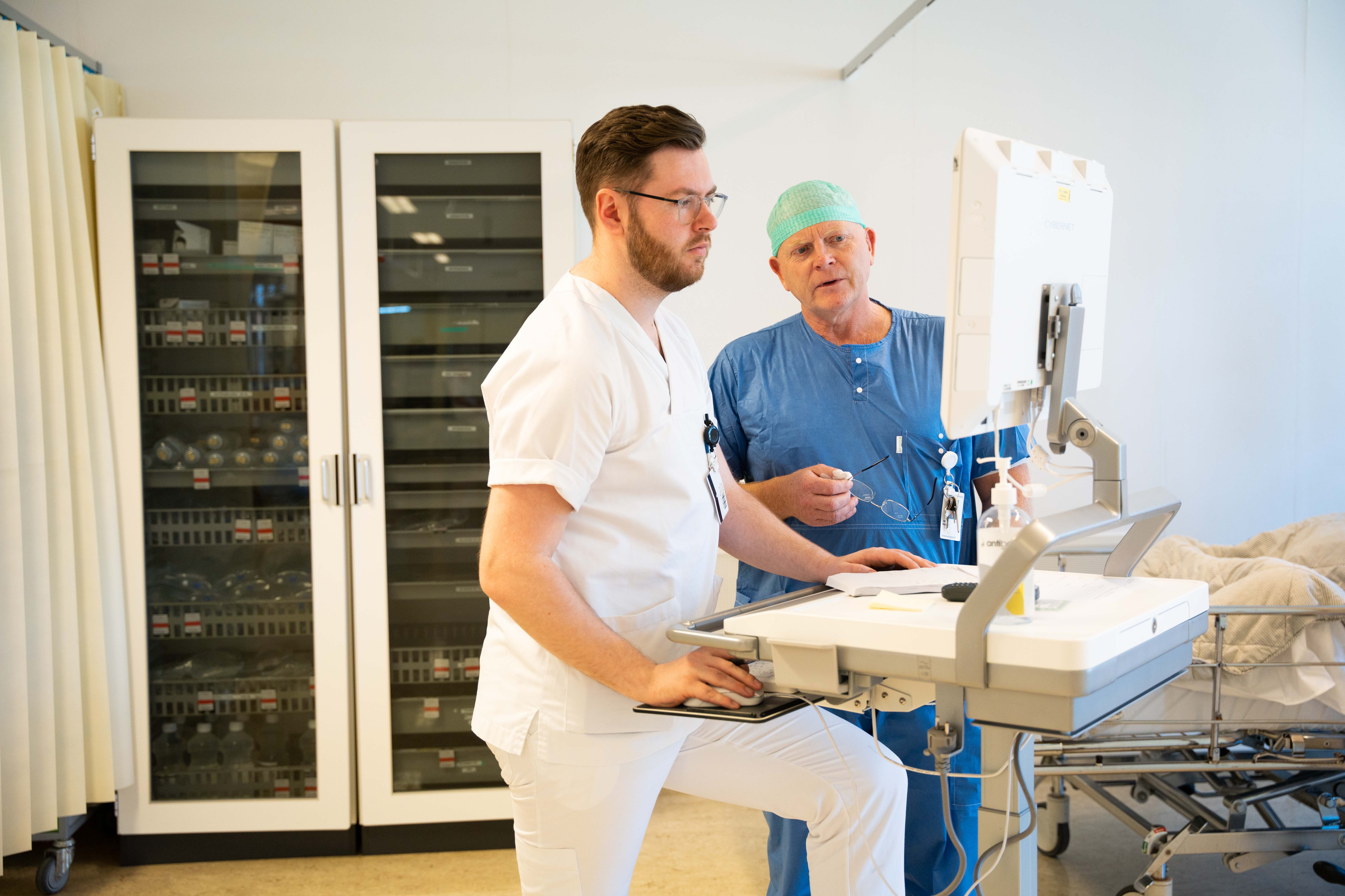 To menn kledd i hvitt og bl&aring;tt samtaler sammen inne p&aring; intenisv.