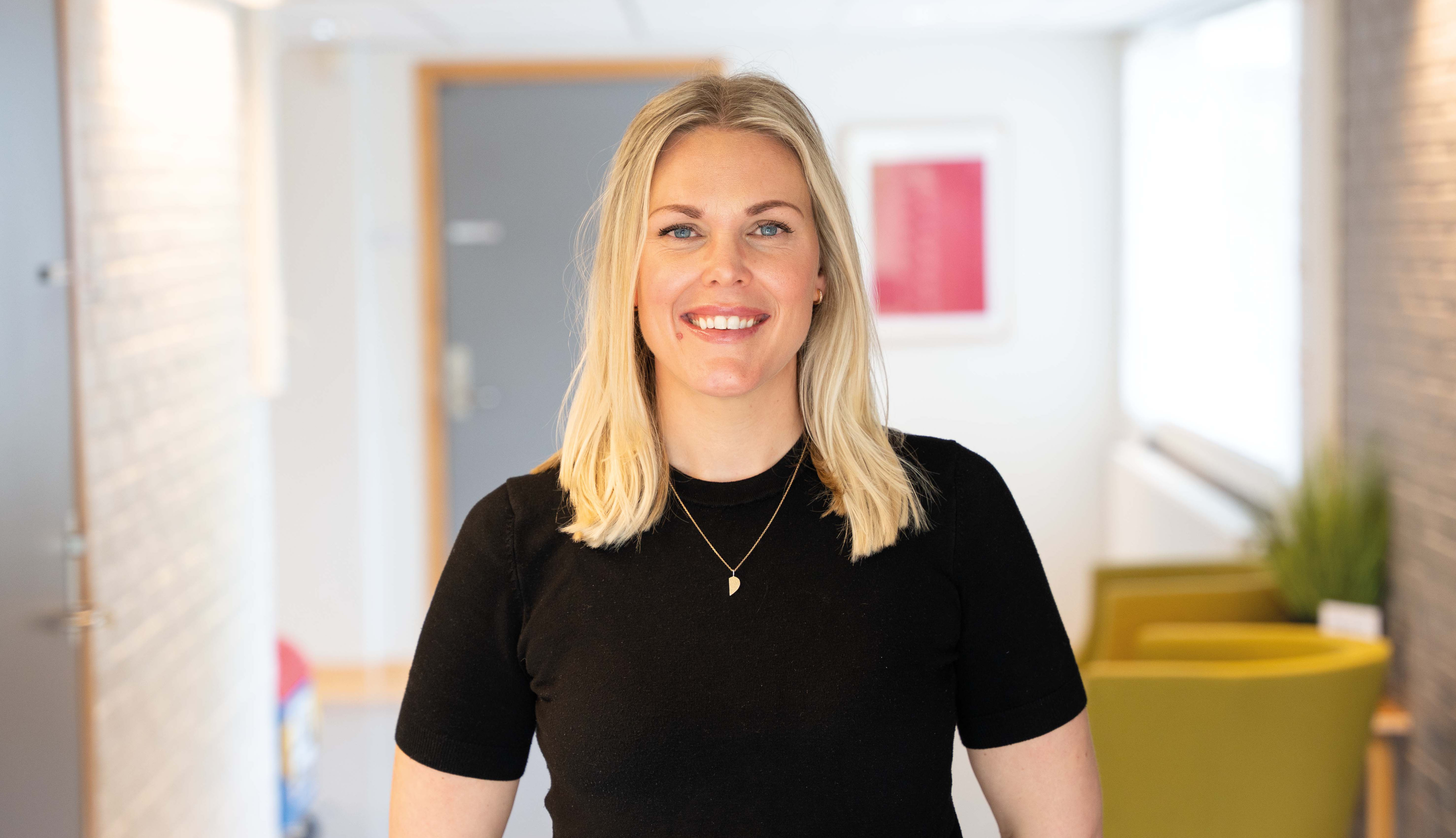 En psykologspesialist st&aring;r smilende i en sykehuskorridor.