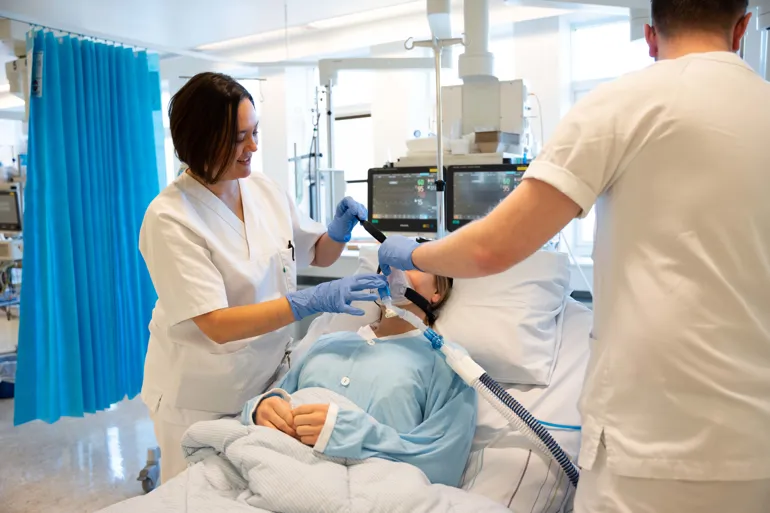 En kvinne kledd i hvitt hejlper en pasient inne på sykehuset.