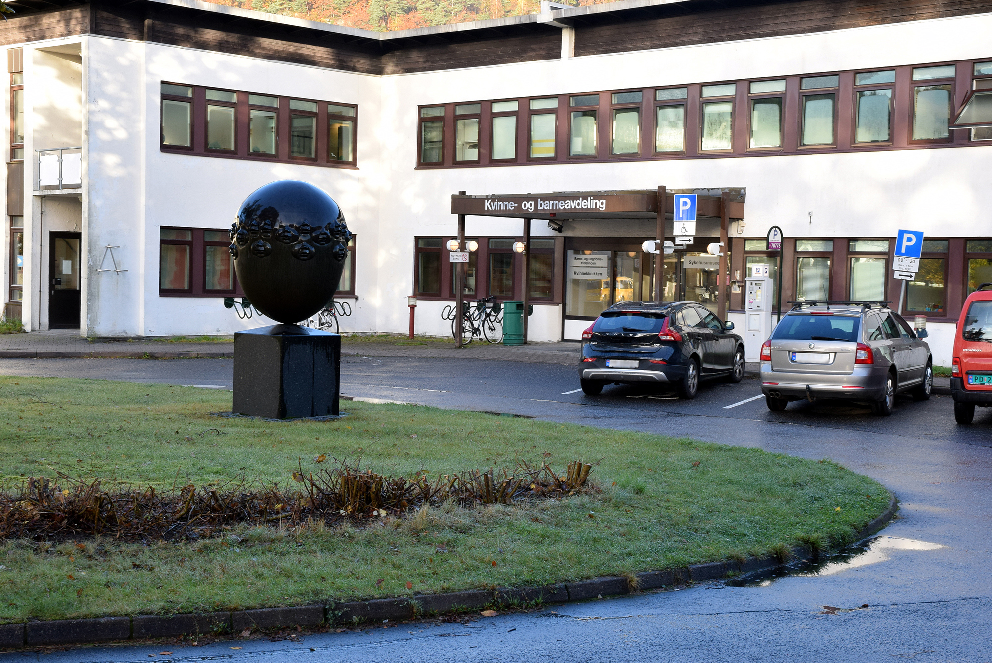 Hvitt murbygg med brune vinduskarmer med parkeringsplasser p&aring; utsiden. Foto