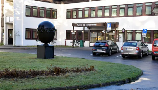 Hvitt murbygg med brune vinduskarmer med parkeringsplasser på utsiden. Foto