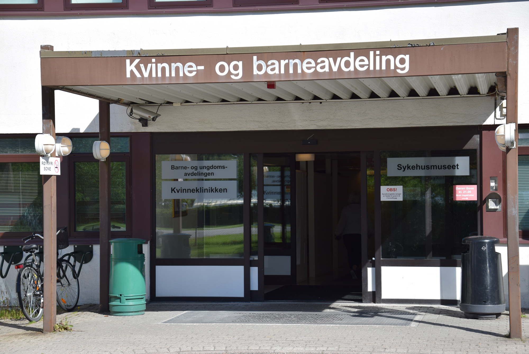 Skilt p&aring; murbygg med skriften Kvinne- og barneavdeling. Inngang under skilt. Foto.